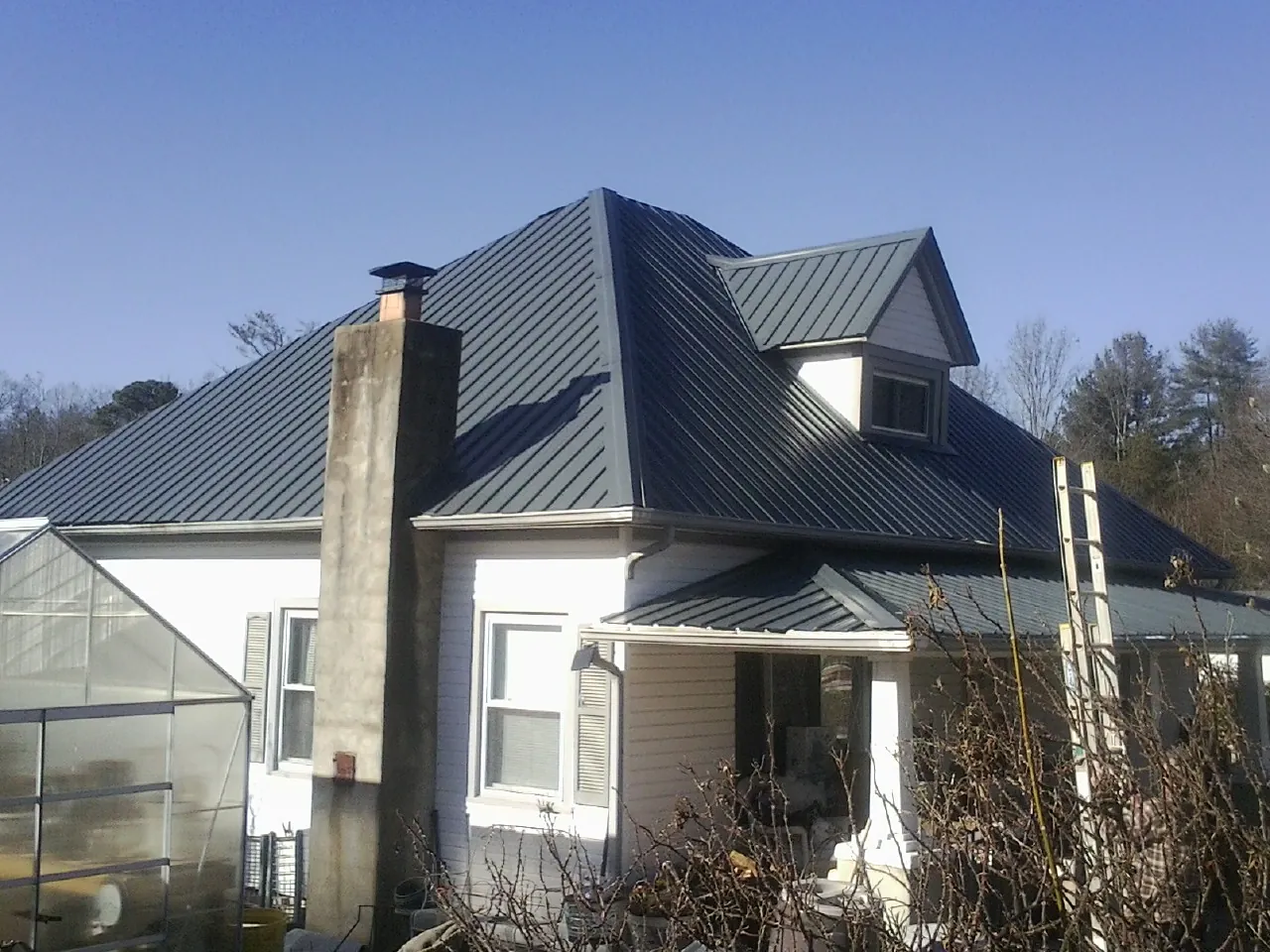 Dark blue standing seam metal roof on a white farmhouse with dormer — Slate & Tile Roof Repair by Roofing Brothers in North Sioux City