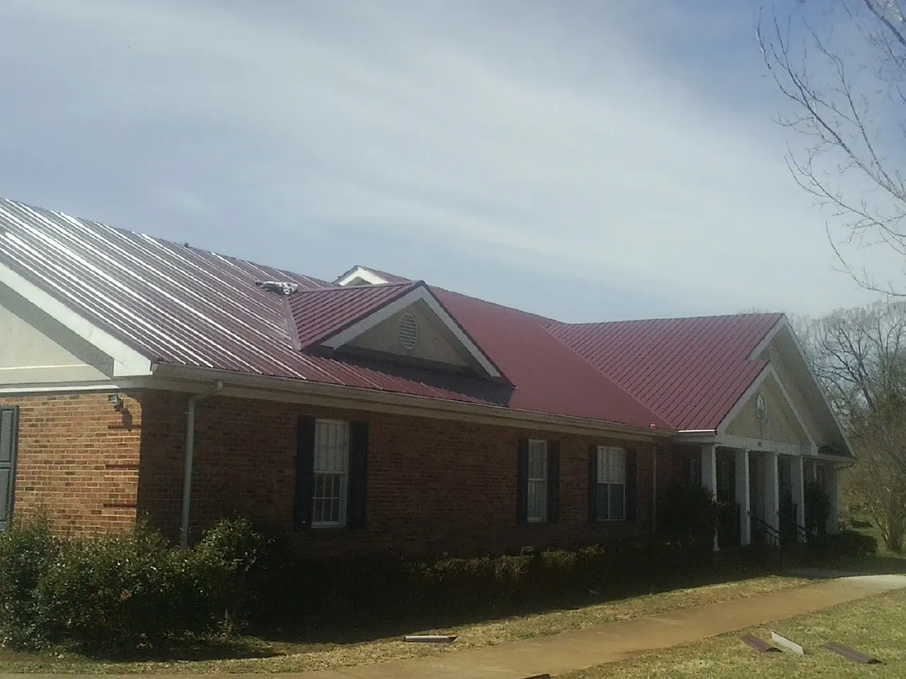 Red metal roof with gabled entries on a long brick building, from a Hail Damage Roof Repair job in North Sioux City