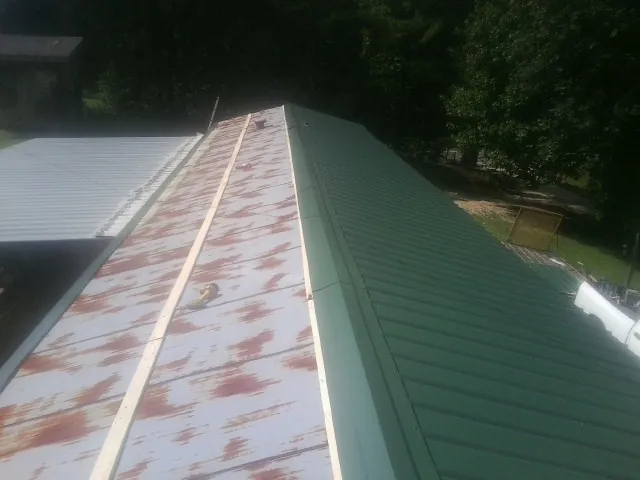 Old rusted panels beside newly installed green metal roofing — Wind Damage Roof Repair by Roofing Brothers in North Sioux City