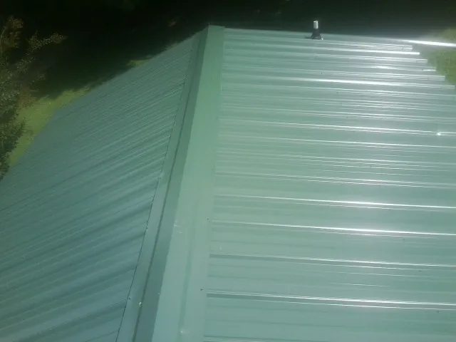 New green metal panels meeting at the ridge of a roof — Flat Roof Repair work by our crew in North Sioux City