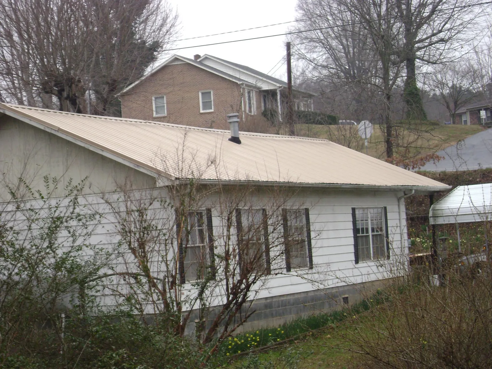 Tan metal roof on a white sided house set into a hillside — Commercial Roofing by Roofing Brothers in North Sioux City